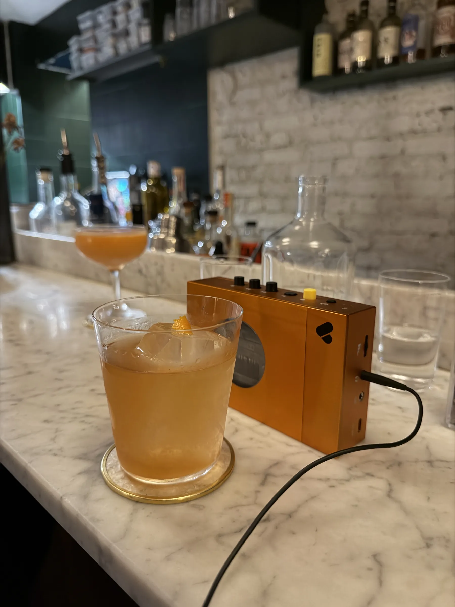 A cocktail on the marble bar at Mesures, Paris, beside a small orange speaker