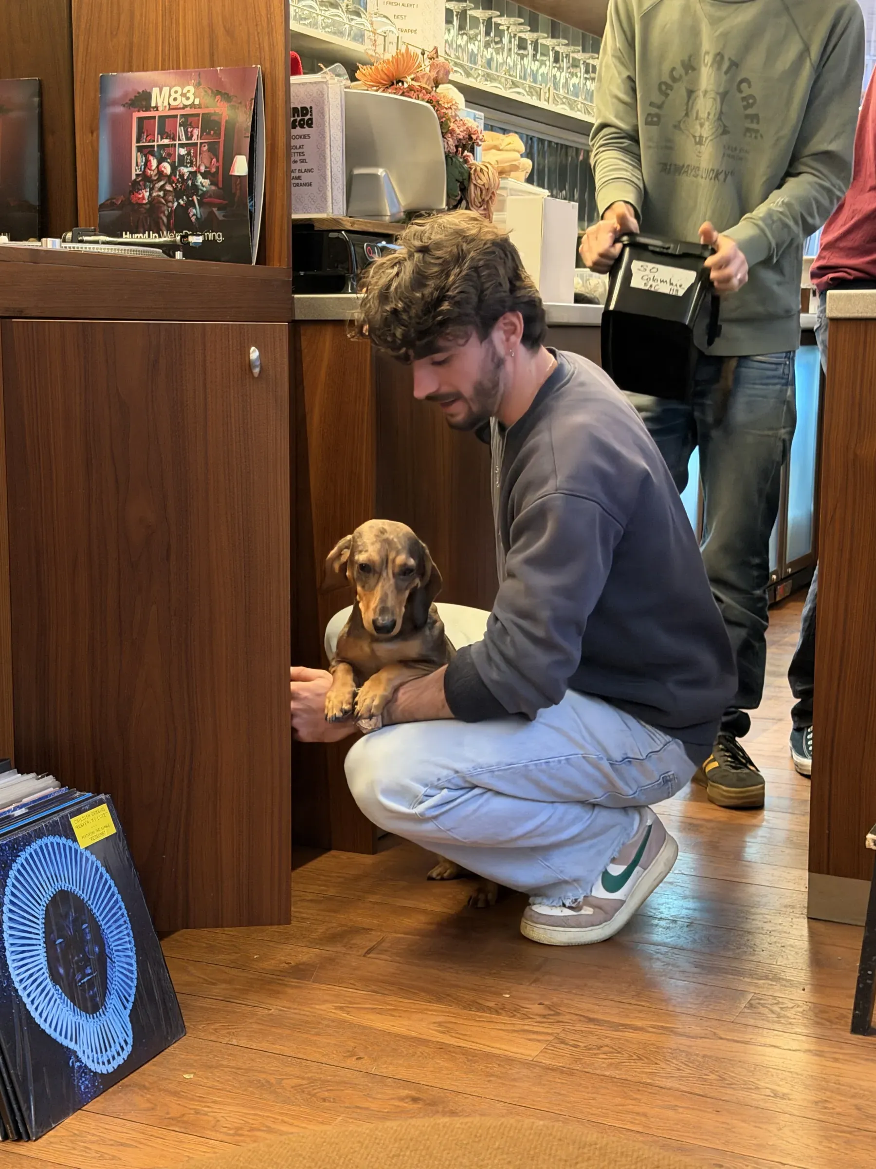 A customer crouching with a dachshund beside the record crates at Sound and Coffee, Paris